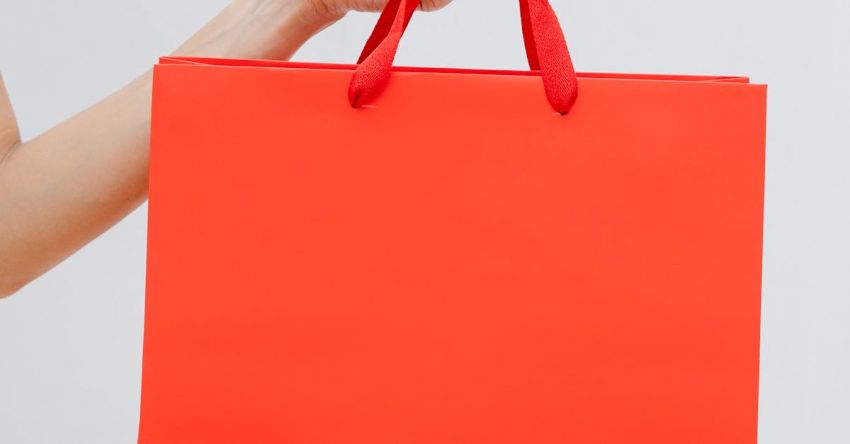 Clearance - Crop unrecognizable female showing red paper shopping bag in hand against white wall